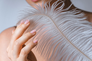 closeup of female hand with smooth skin and soft ostrich feather